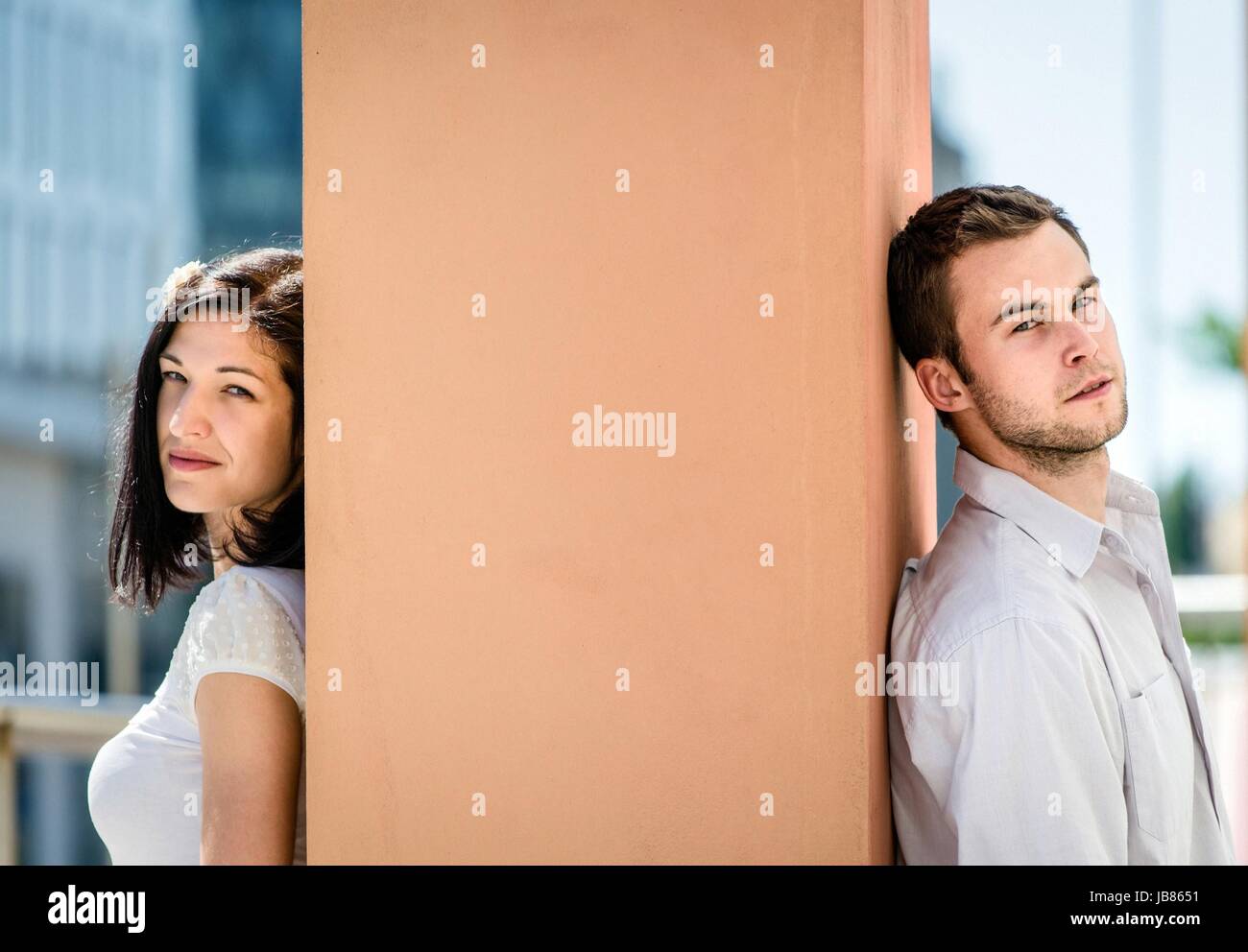 Two people sitting on opposite side of big collumn outdoor in street
