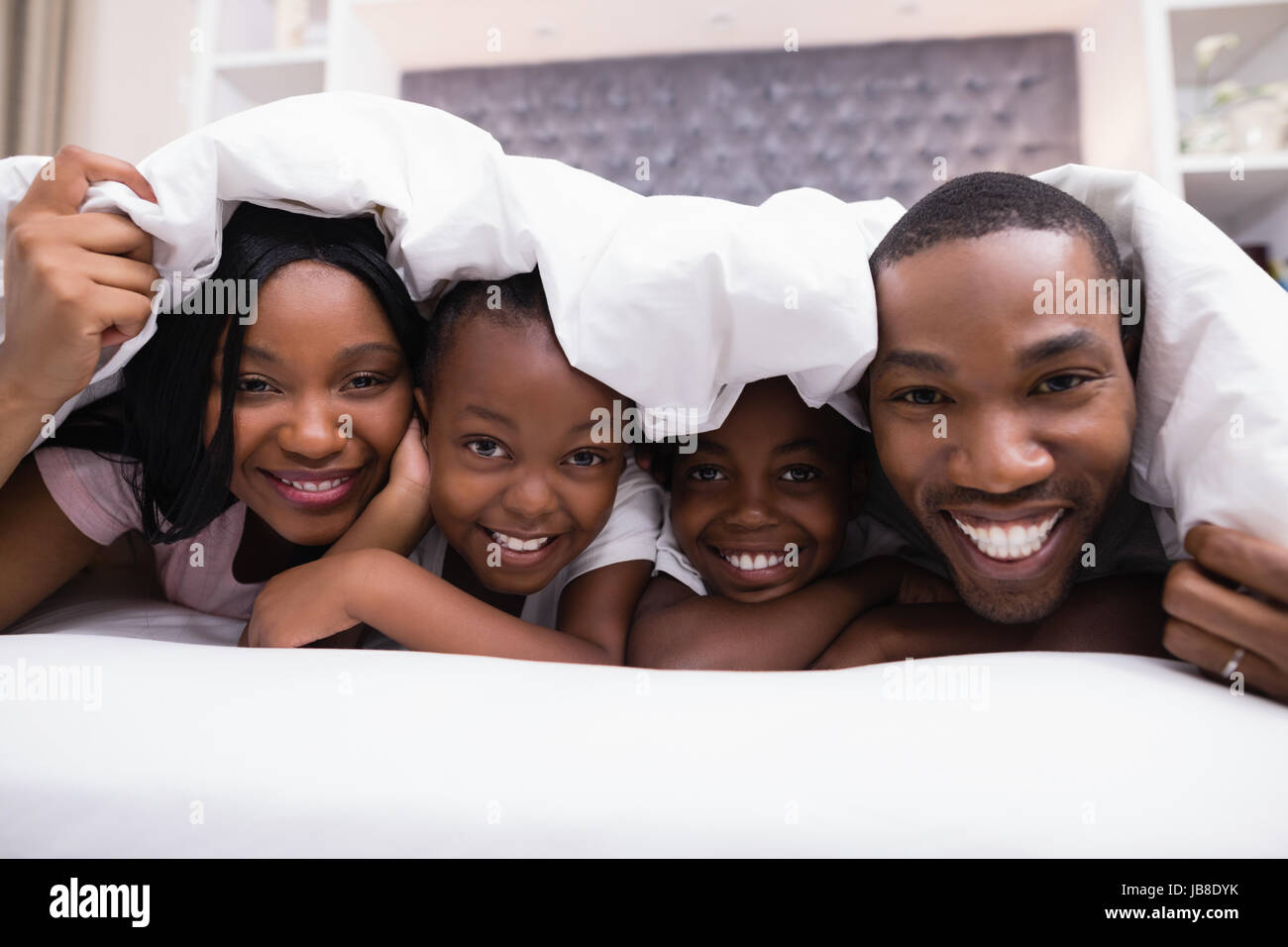 Close up portrait of happy family lying together under blanket on bed ...