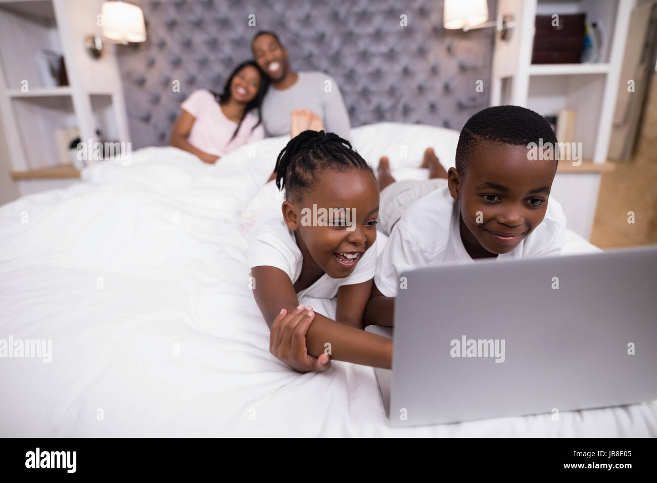 Happy siblings using laptop on bed with parents sitting in background at home Stock Photo