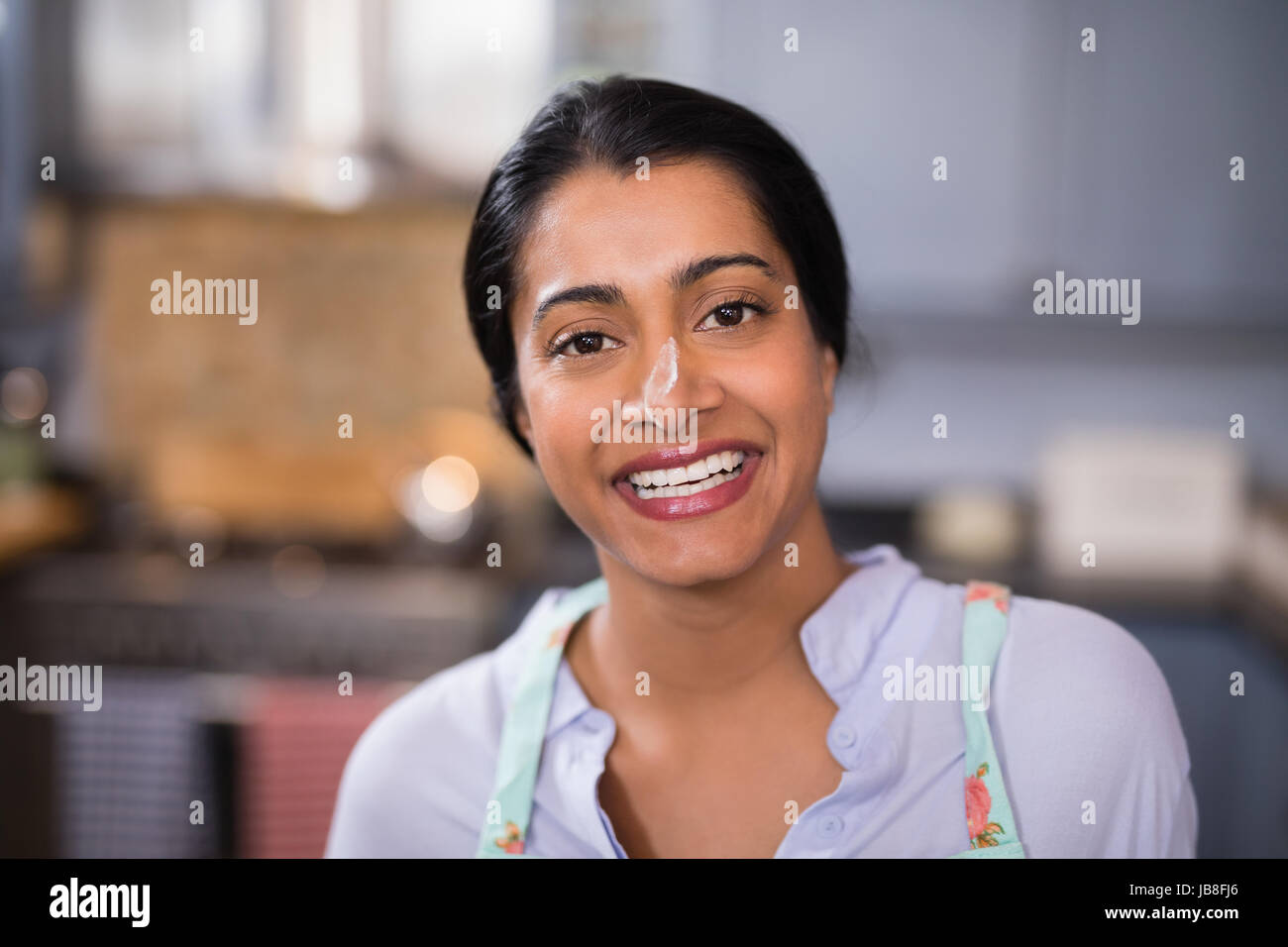 Portrait of happy young woman with flour on nose in kitchen at home Stock Photo