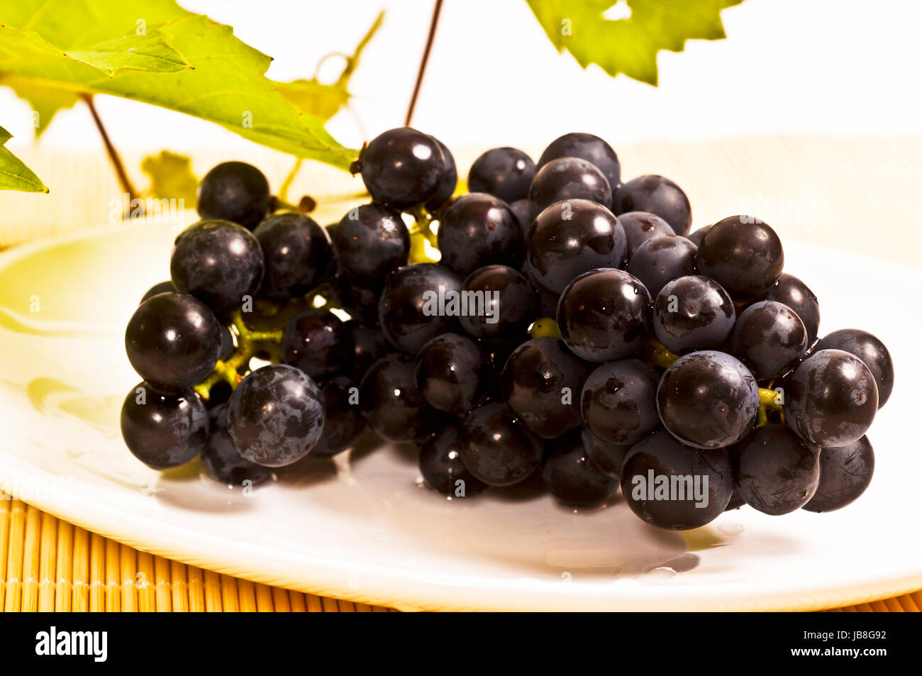 frische rote Weintrauben mit Weinlaub auf weißem Hintergrund Stock Photo