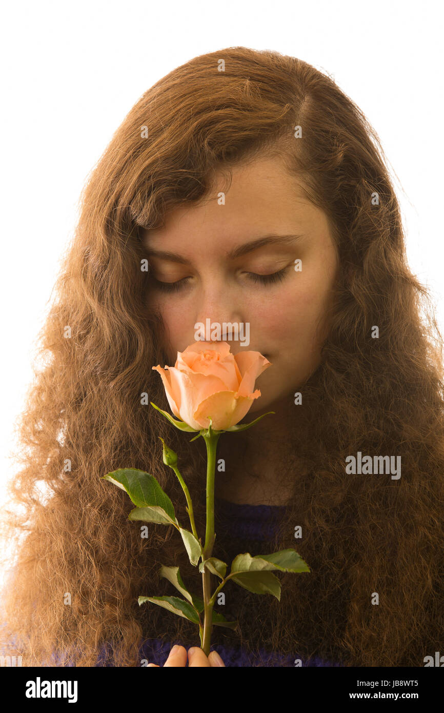 Eine junge hübsche Frau hält eine Rose in der Hand und riecht daran Stock Photo