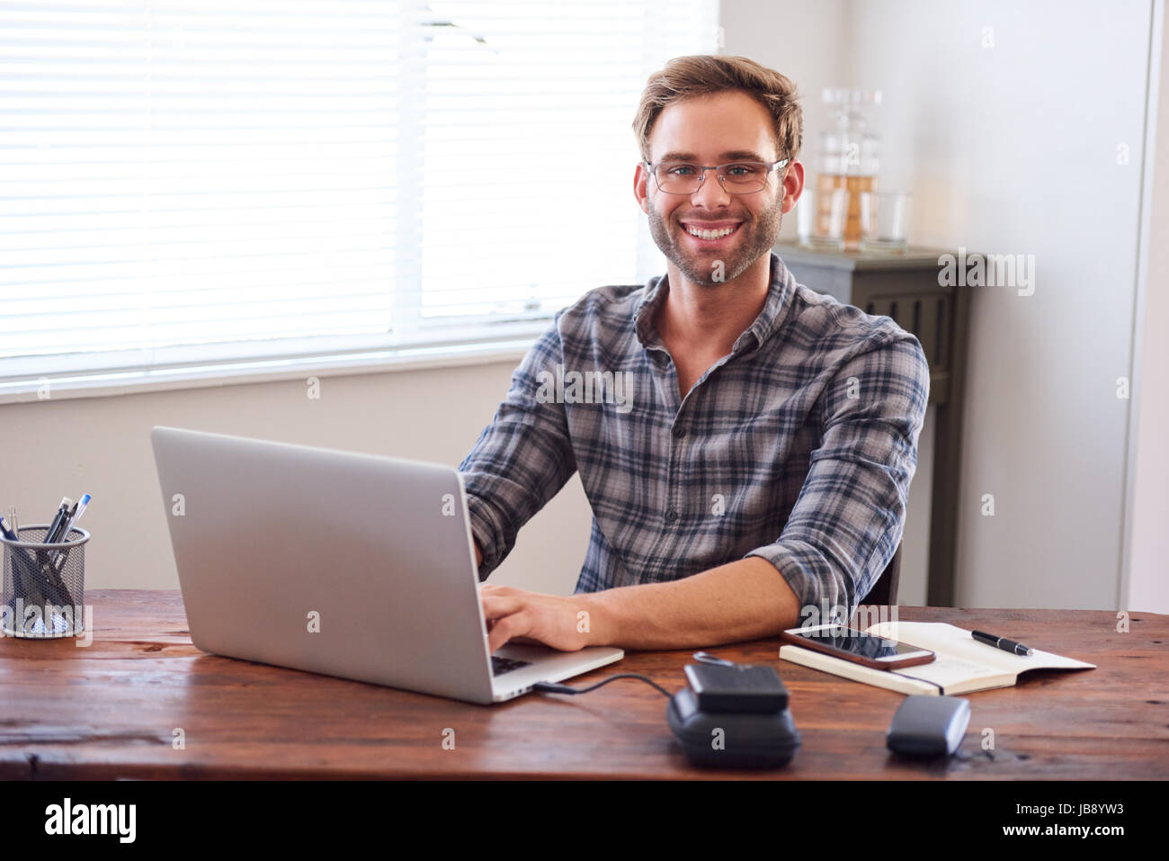 Attractive young, well groomed caucasian male entrepreneur and businessman smiling at the camera with his hands on the keyboard of his laptop computer Stock Photo