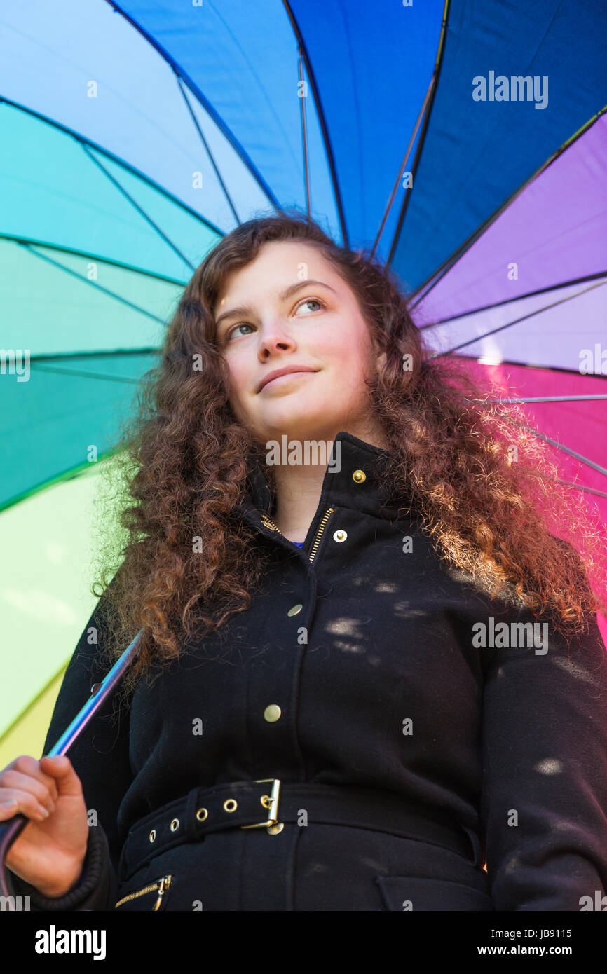 Eine junge hübsche Frau steht mit einem bunten Schirm in der Wintersonne Stock Photo