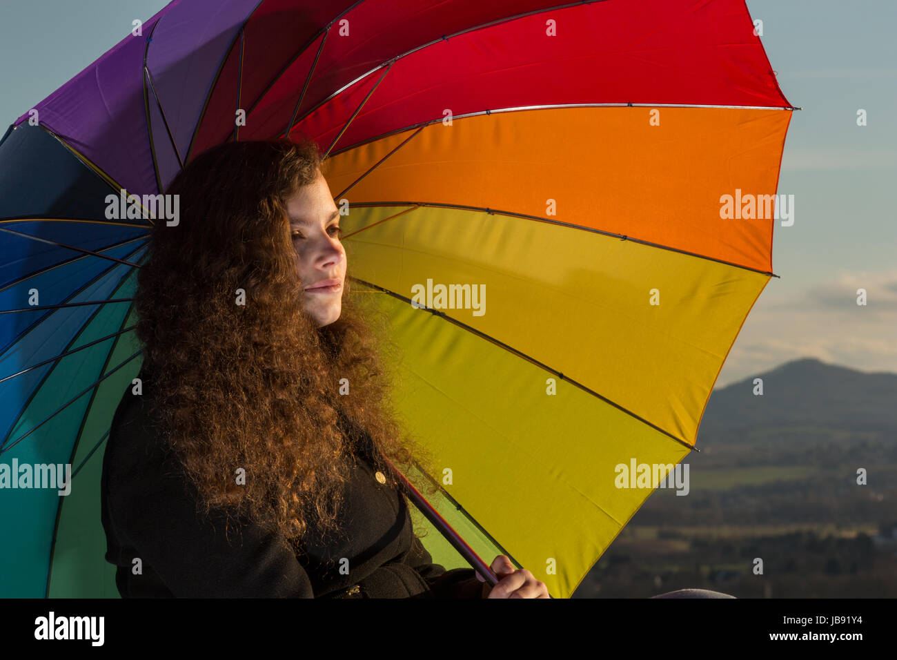 Eine junge hübsche Frau sitzt mit einem bunten Schirm in der Wintersonne Stock Photo