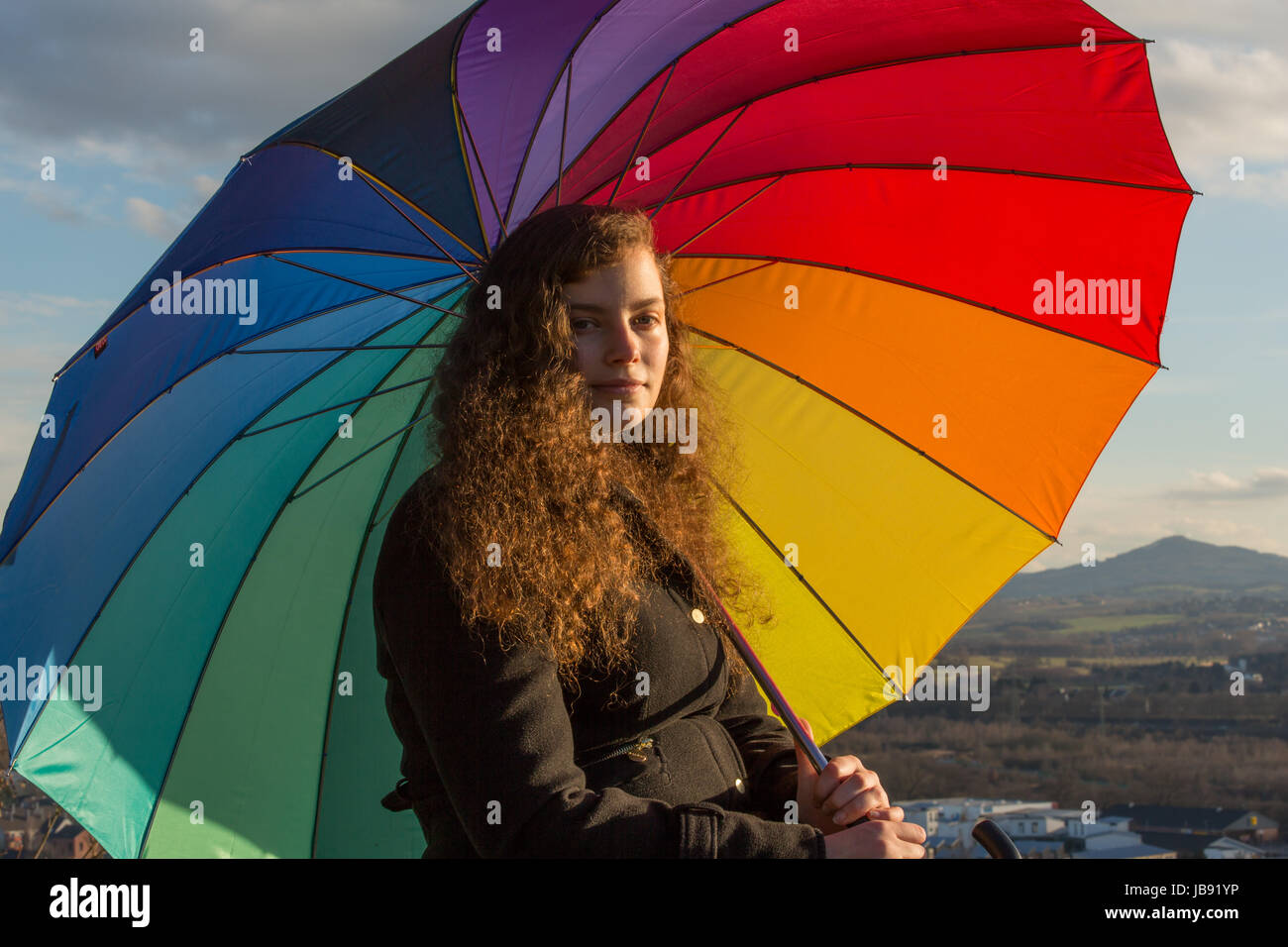 Eine junge hübsche Frau sitzt mit einem bunten Schirm in der Wintersonne Stock Photo