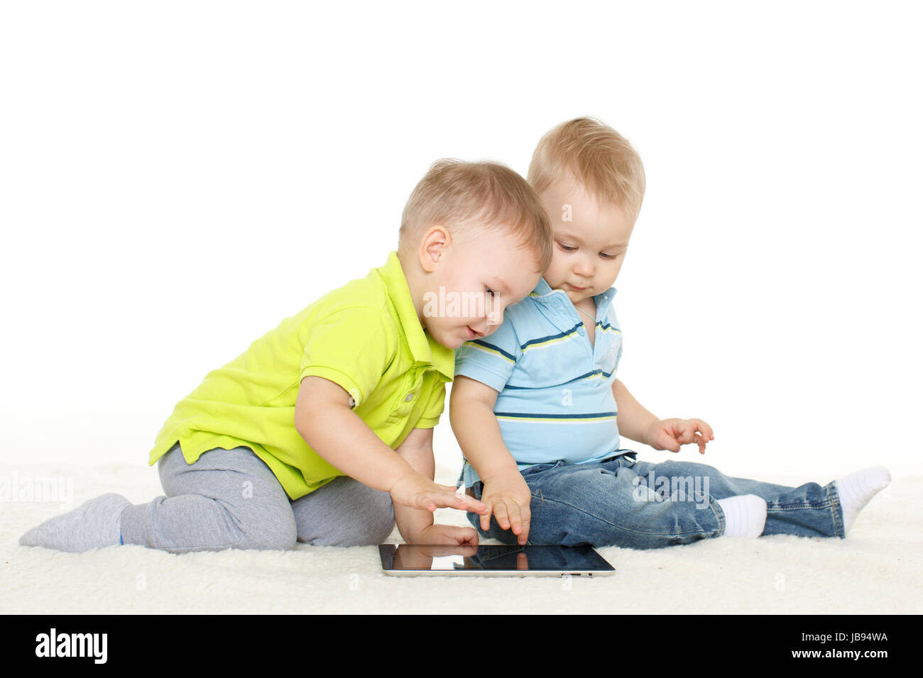 Two little boys with computer tablet  sit on a floor on a white background. Stock Photo