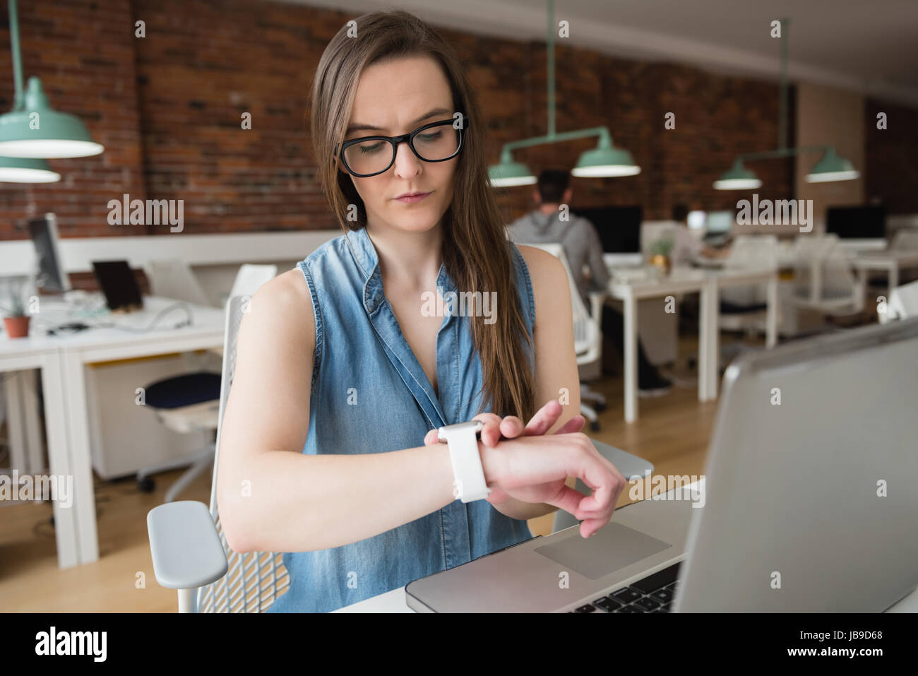Female executive adjusting smart watch at desk in office Stock Photo
