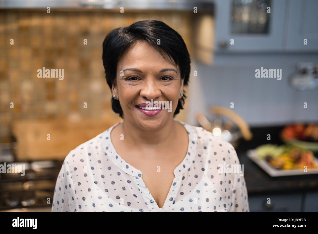 Portrait of smiling mature woman standing in kitchen at home Stock Photo