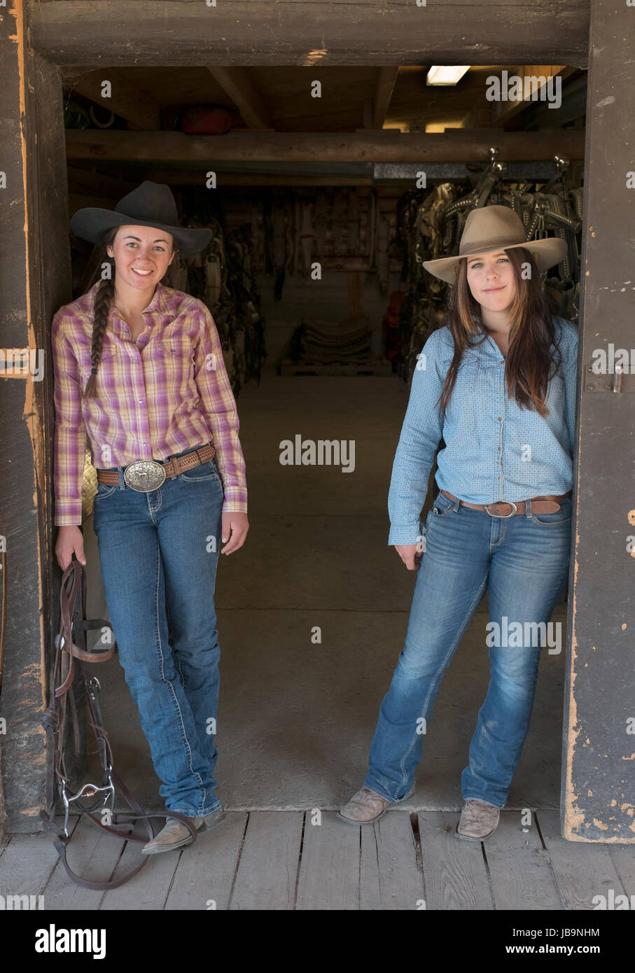 Two young female "Dude Ranchers" pose for a photograph outside the tack room at the Heart Six Ranch, near Moran junction, Wyoming, USA. Stock Photo