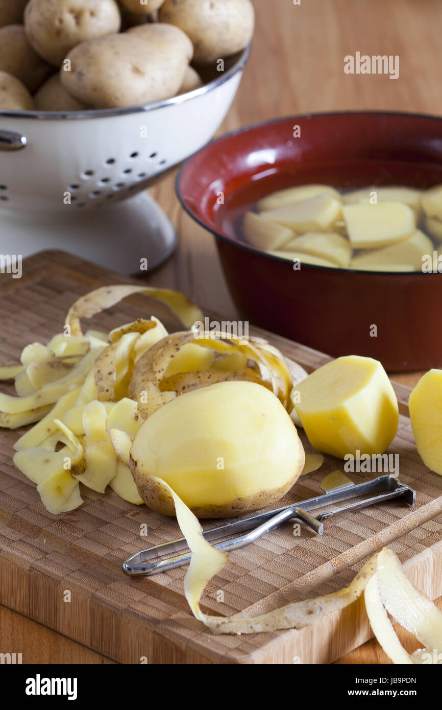 Kartoffeln und Kartoffelschäler auf Schneidebrett Stock Photo