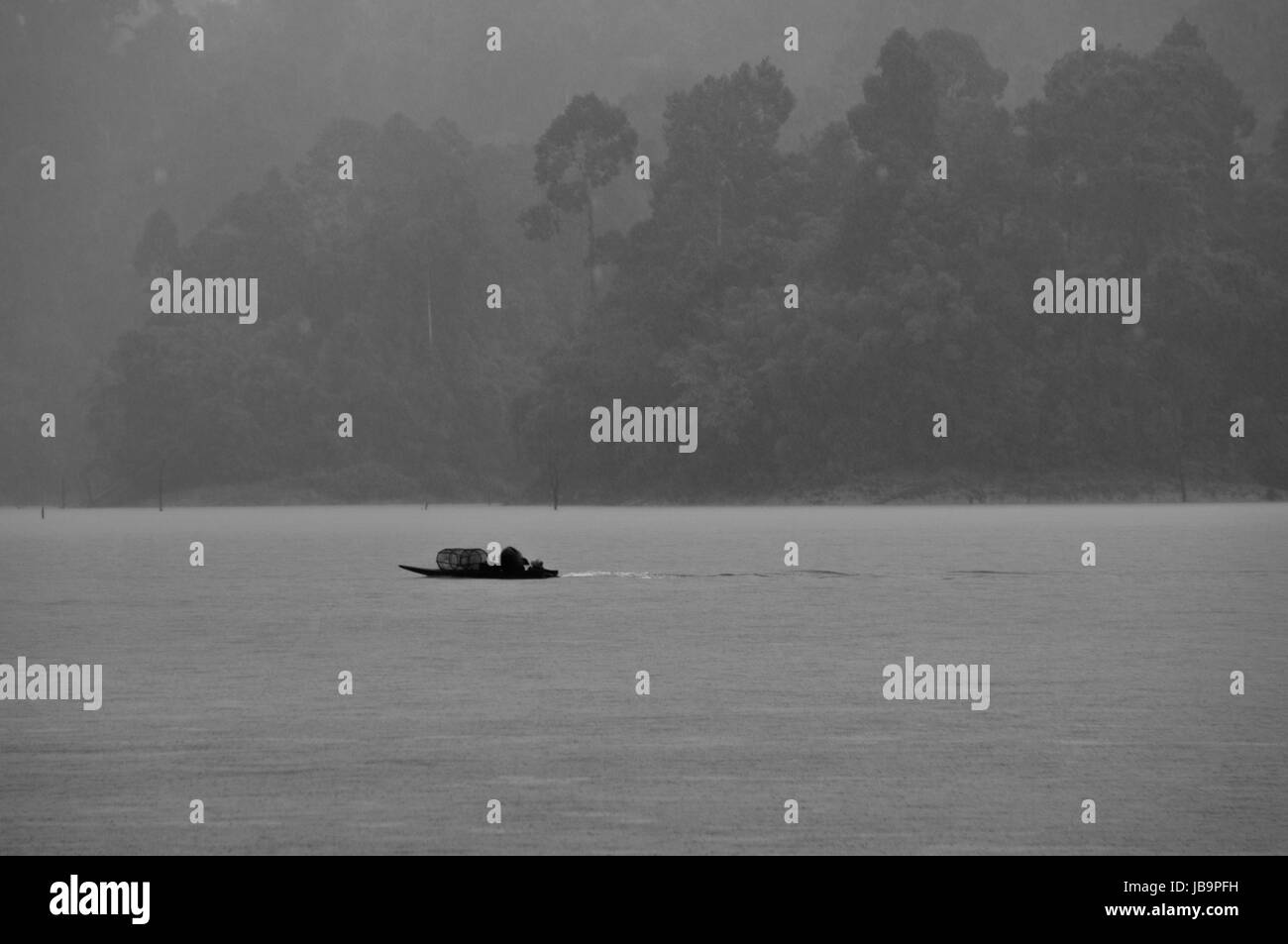 A small boat navigating the Cheow Lan Lake in a tropical rain (black and white) Stock Photo