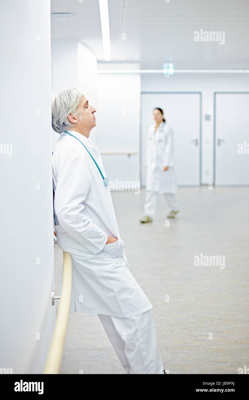 müder Arzt an Wand lehnend im Krankenhaus Stock Photo