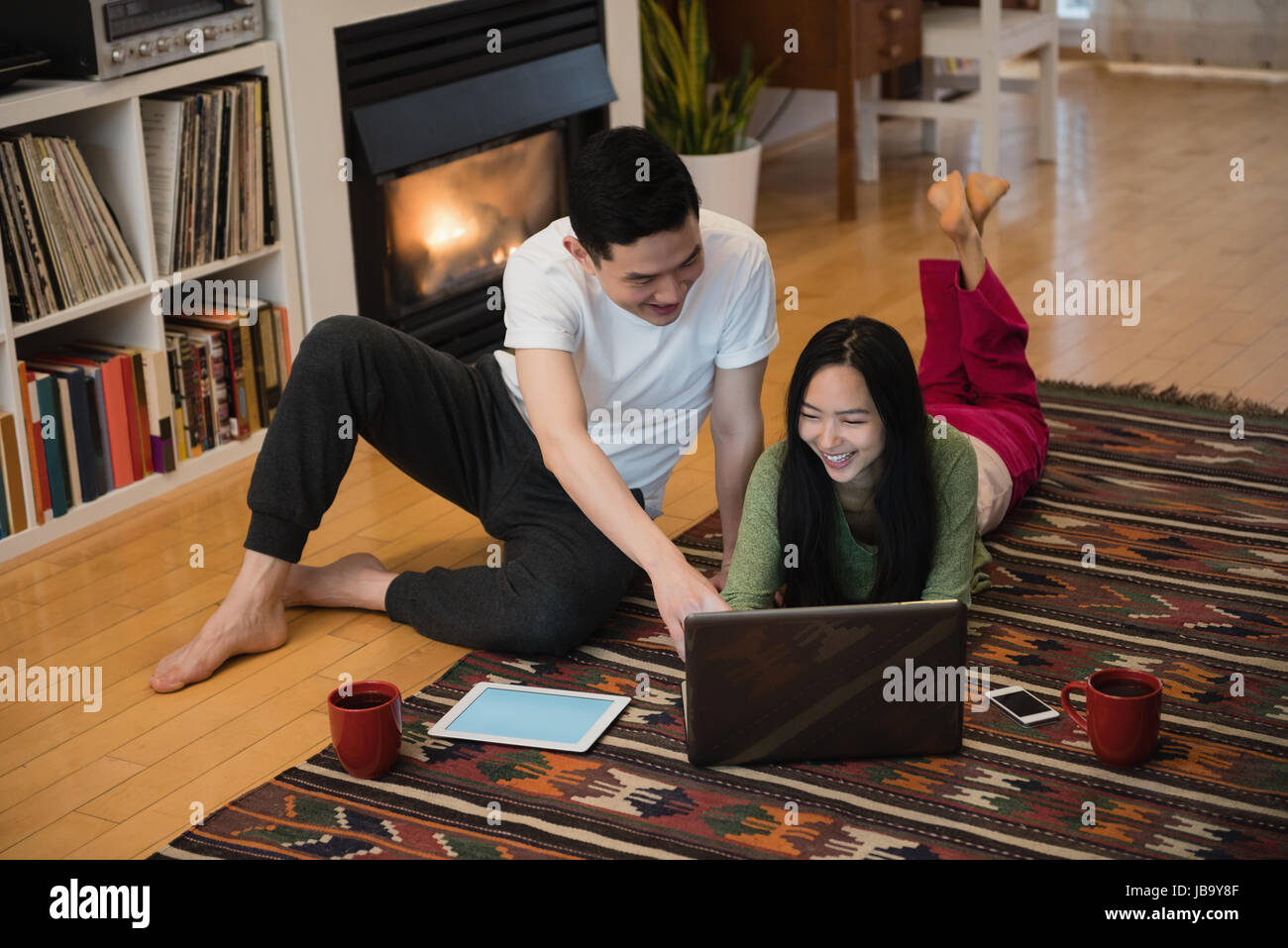 Happy couple using laptop near fireplace in living room at home Stock ...