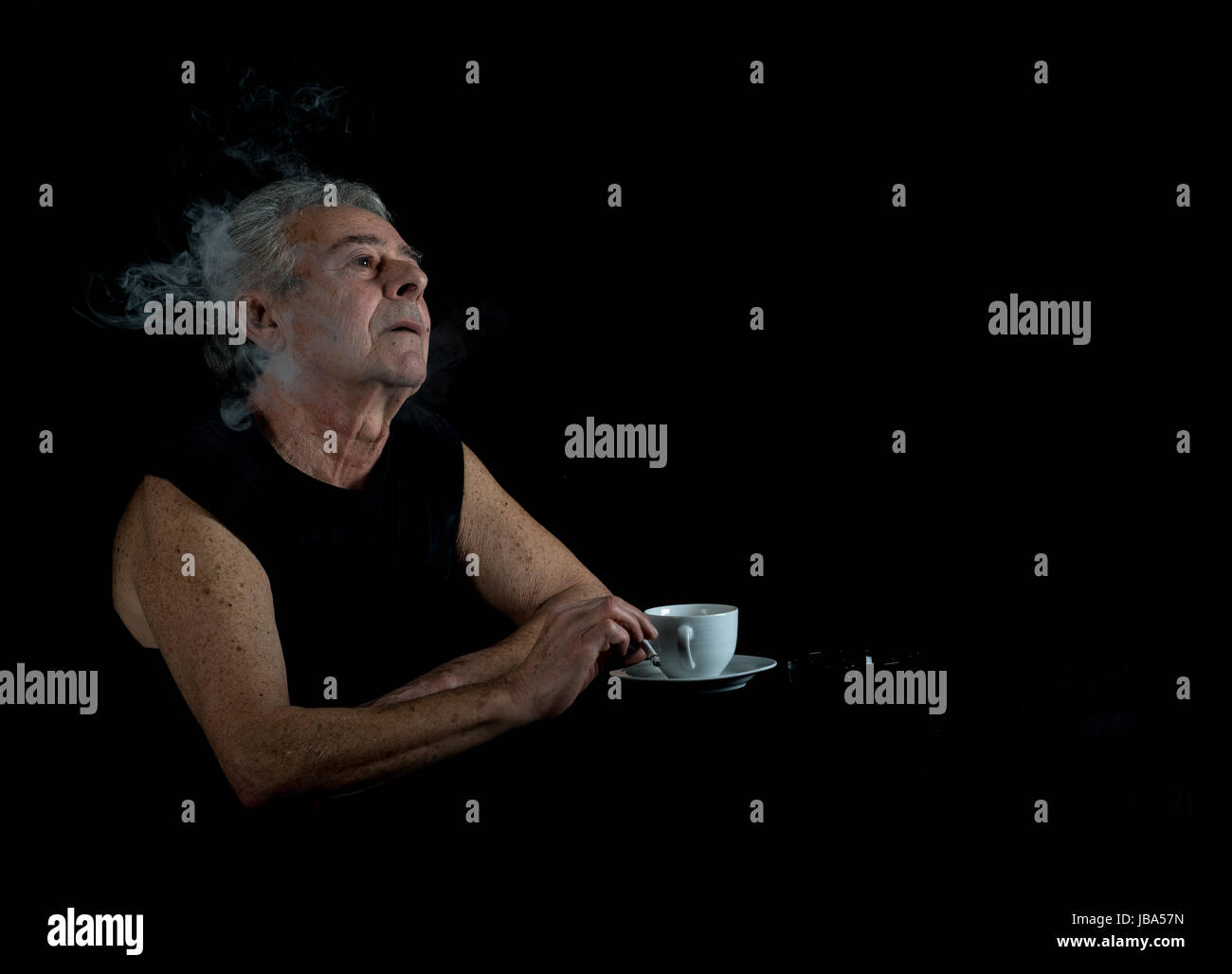 Alter Mann sitzt am Tisch und raucht eine Zigarette Stock Photo