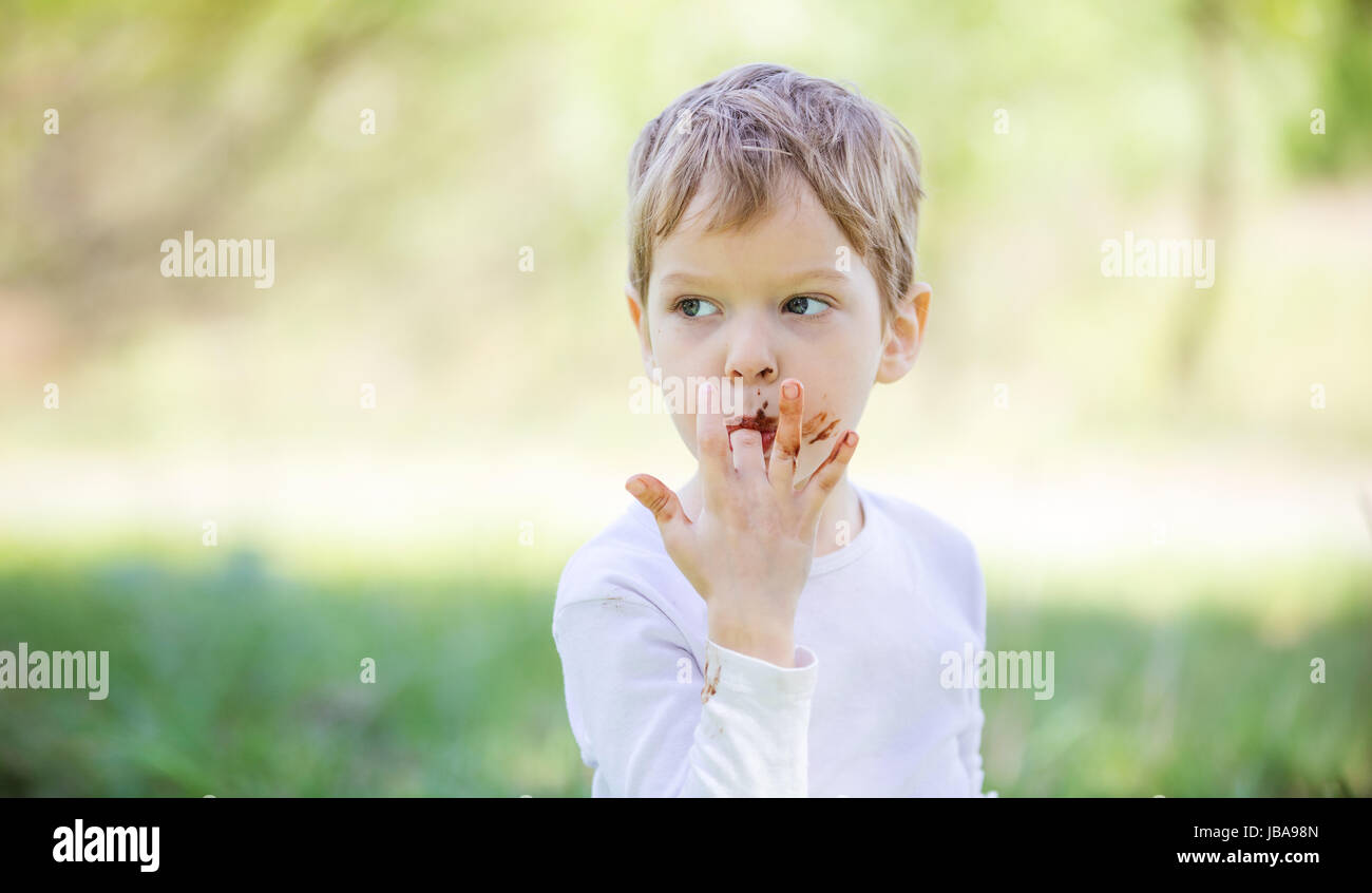 Cute little boy licking fingers while eating chocolate outdoors Stock Photo