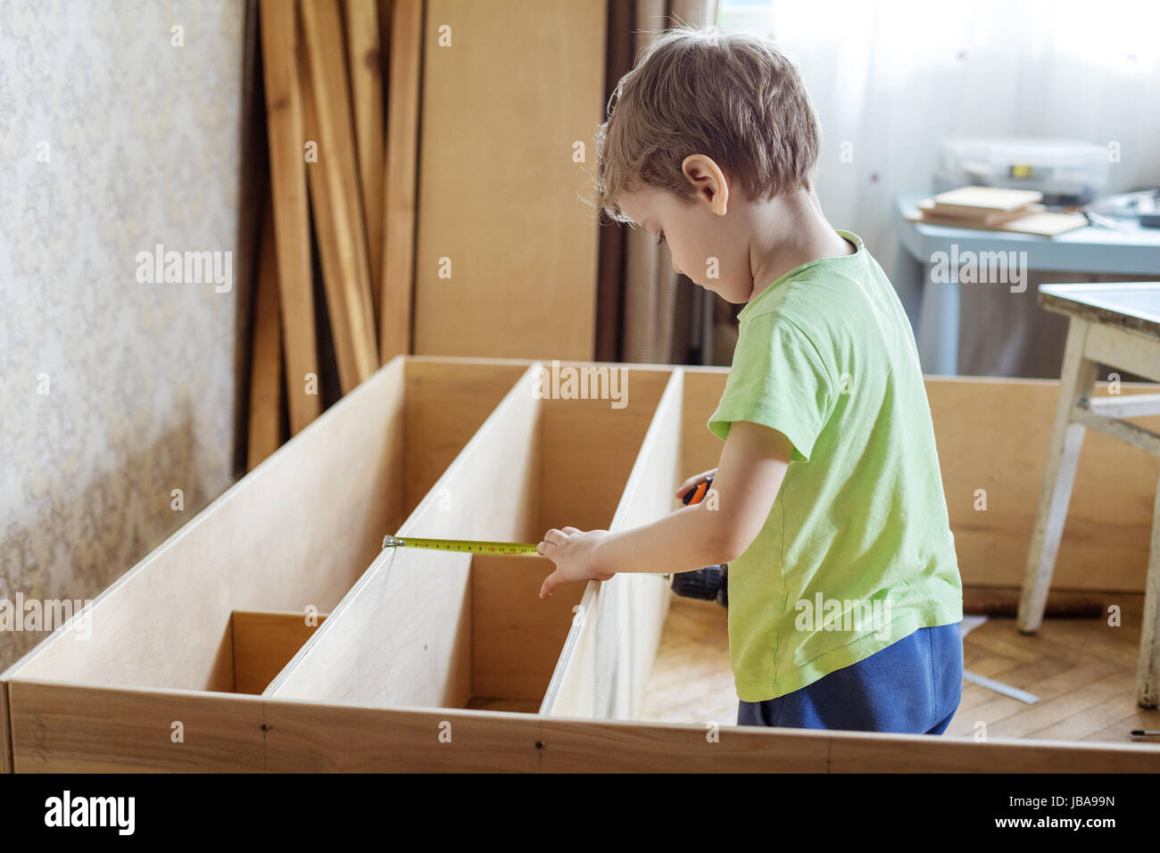 Young boy using reel to measure wooden shelf of bookcase or shelf unit Stock Photo