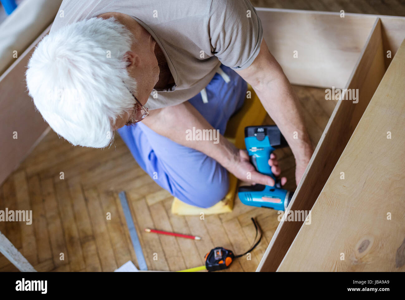 Mature man using electric screwdriver while making bookcase or shelf unit, view from above Stock Photo