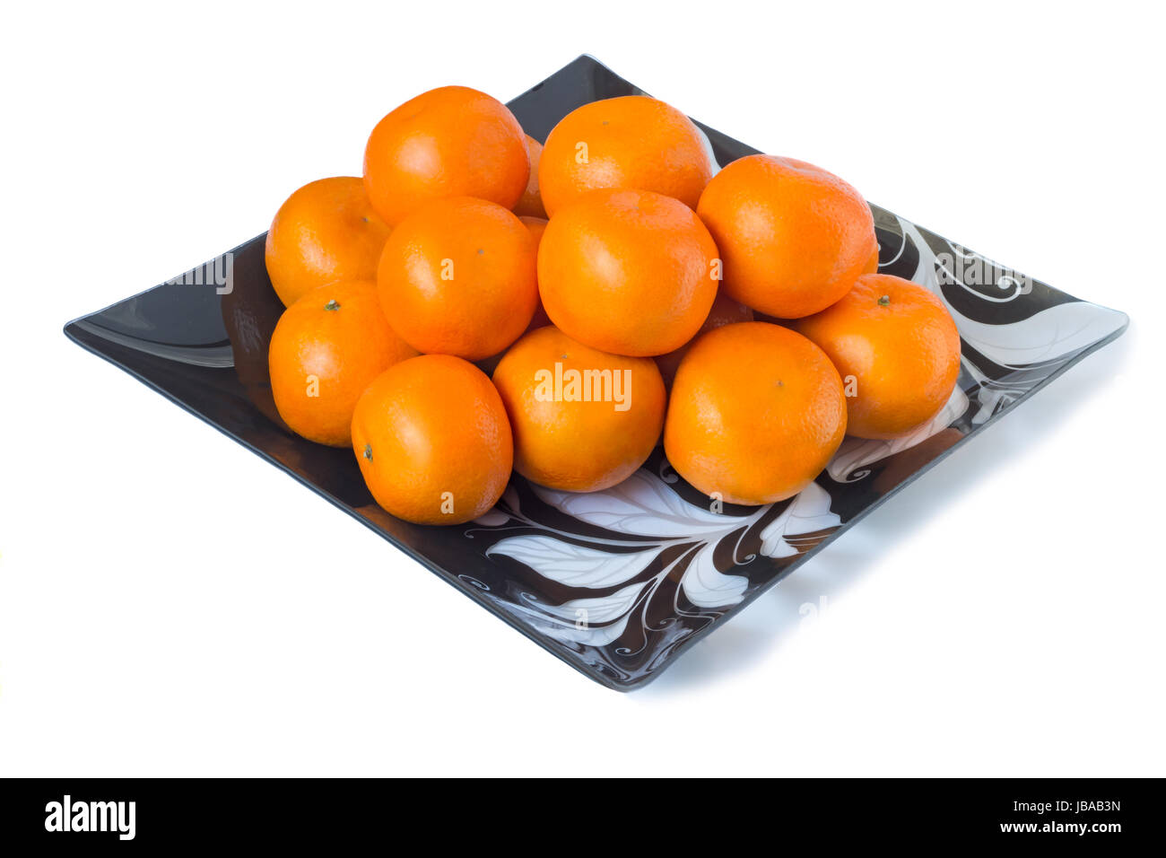 Large ripe oranges are located on a dish made of dark glass with ornament. Presented on a white background Stock Photo