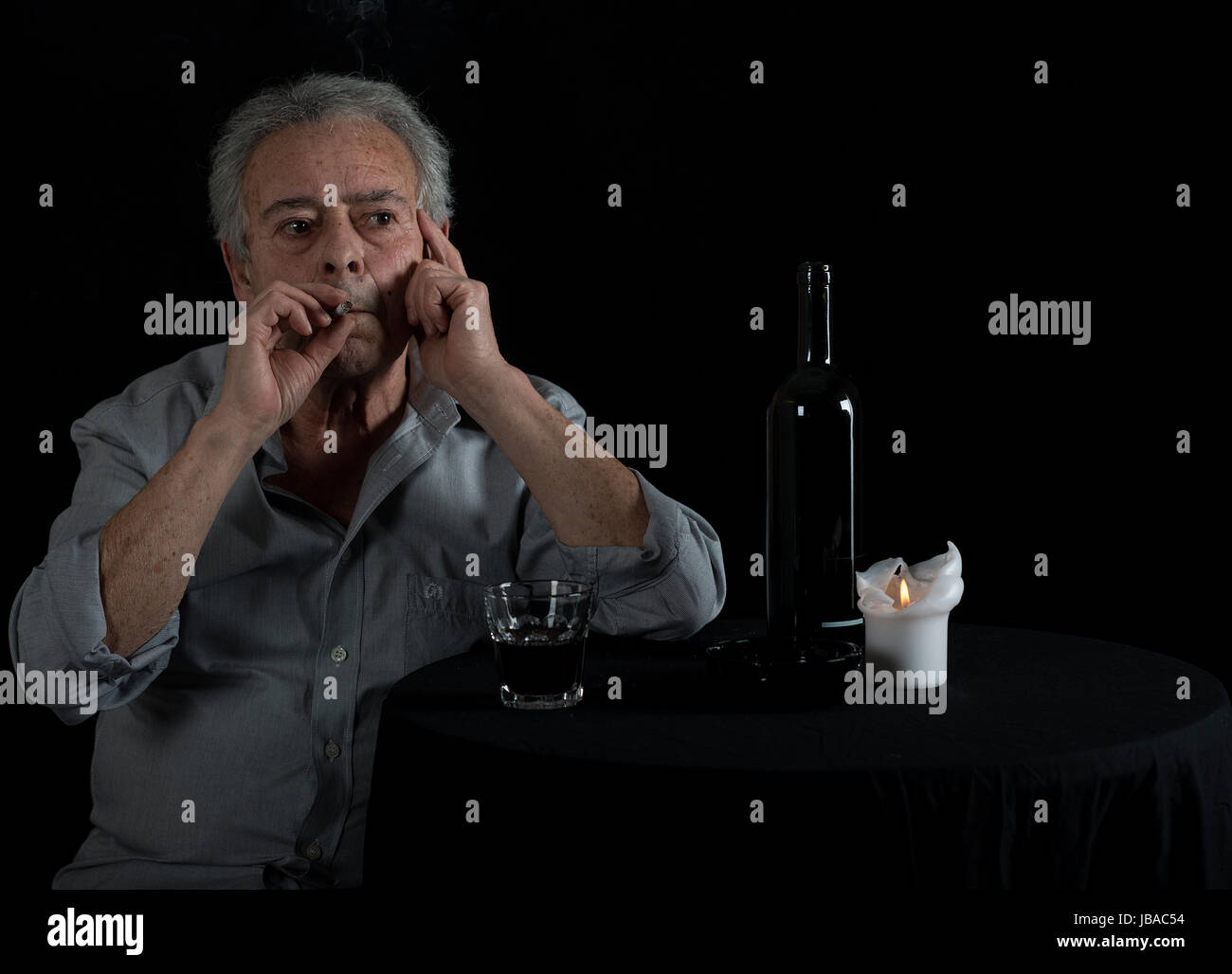 Alter Mann sitzt am Tisch und trinkt Wein und raucht eine Zigarette Stock Photo