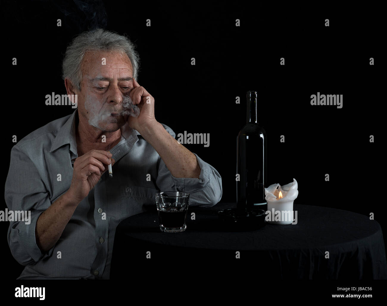 Alter Mann sitzt am Tisch und trinkt Wein und raucht eine Zigarette Stock Photo