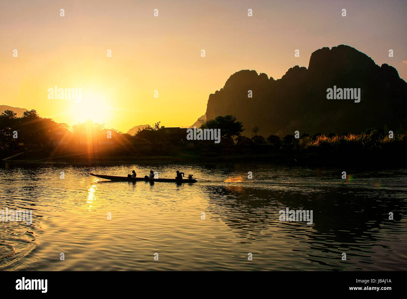 Sunset over Nam Song River with silhouetted rock formations and a boat in Vang Vieng, Laos. Vang Vieng is a popular destination for adventure tourism  Stock Photo