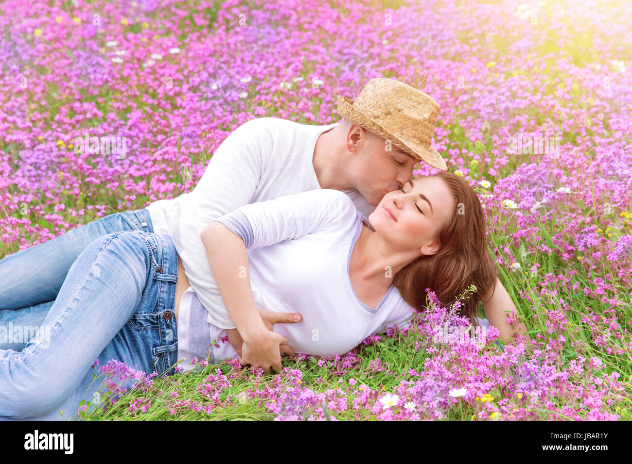 Beautiful cheerful couple lying down on floral glade and kissing ...