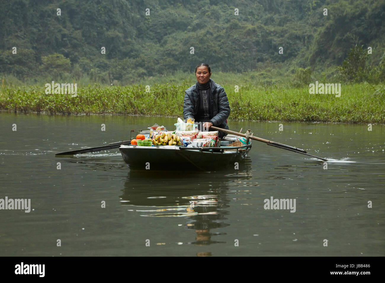 Hawker with floating shop on Tam Coc (three caves) boat trip through limestone karsts on Ngo Dong River, (UNESCO World Herritage Area), near Ninh Binh Stock Photo