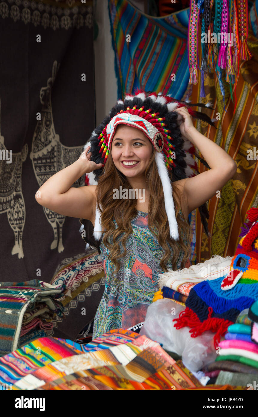 A beautiful young woman wearing Native American hat feather. with colorful fabrics background. Stock Photo