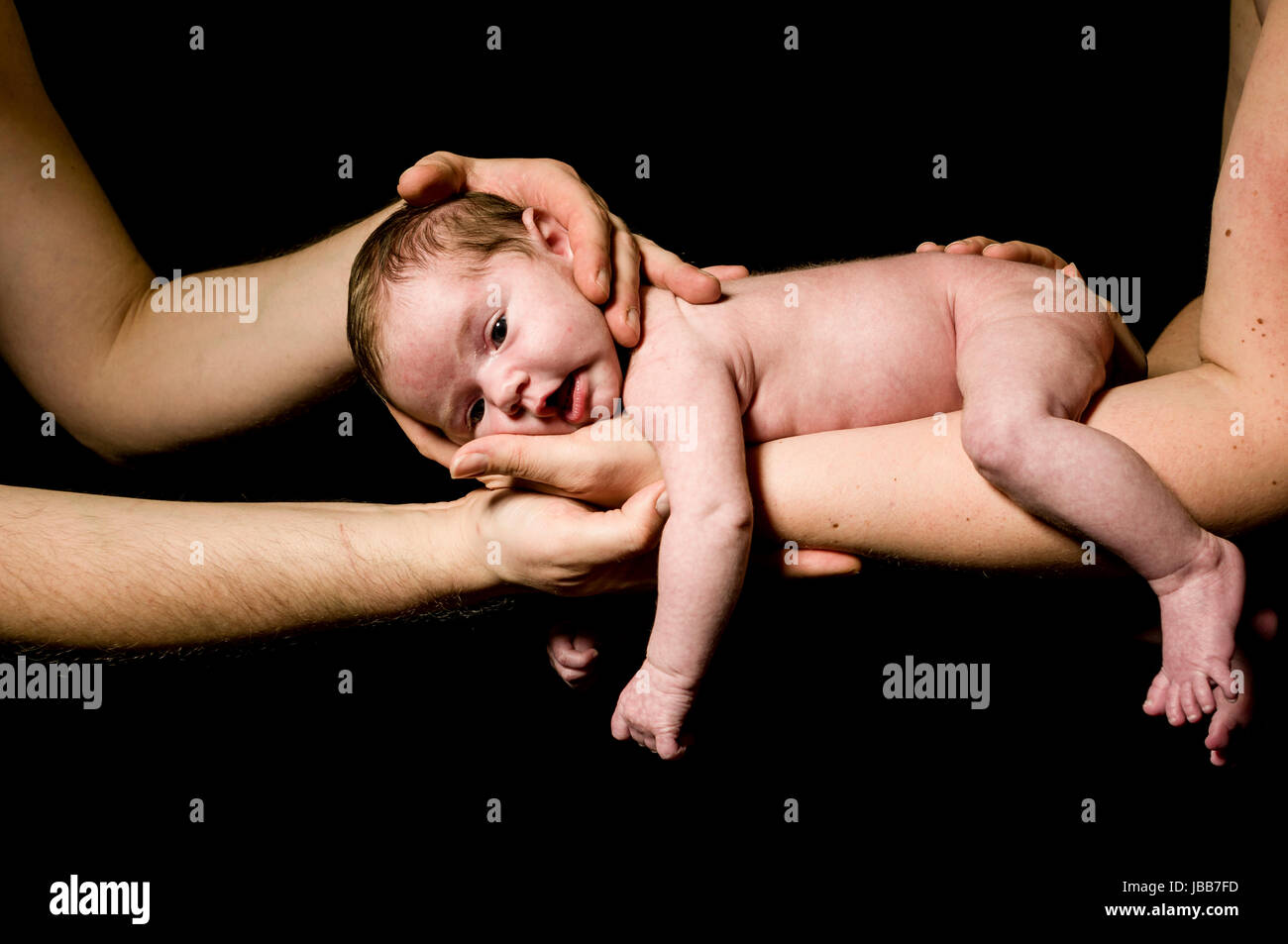 Ein kleines neugeborenes Baby wird auf der Hand der Mutter getragen und von Vaters Haenden beschuetzt und schaut zufrieden aus, freigestellt vor schwarzem Hintergrund. Stock Photo