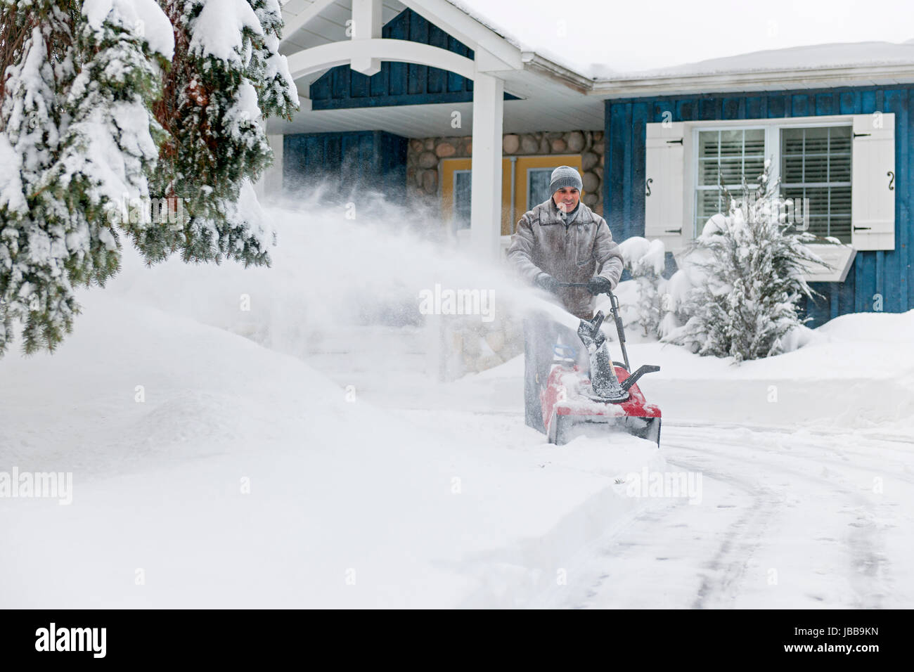 Man using snowblower to clear deep snow on driveway near residential
