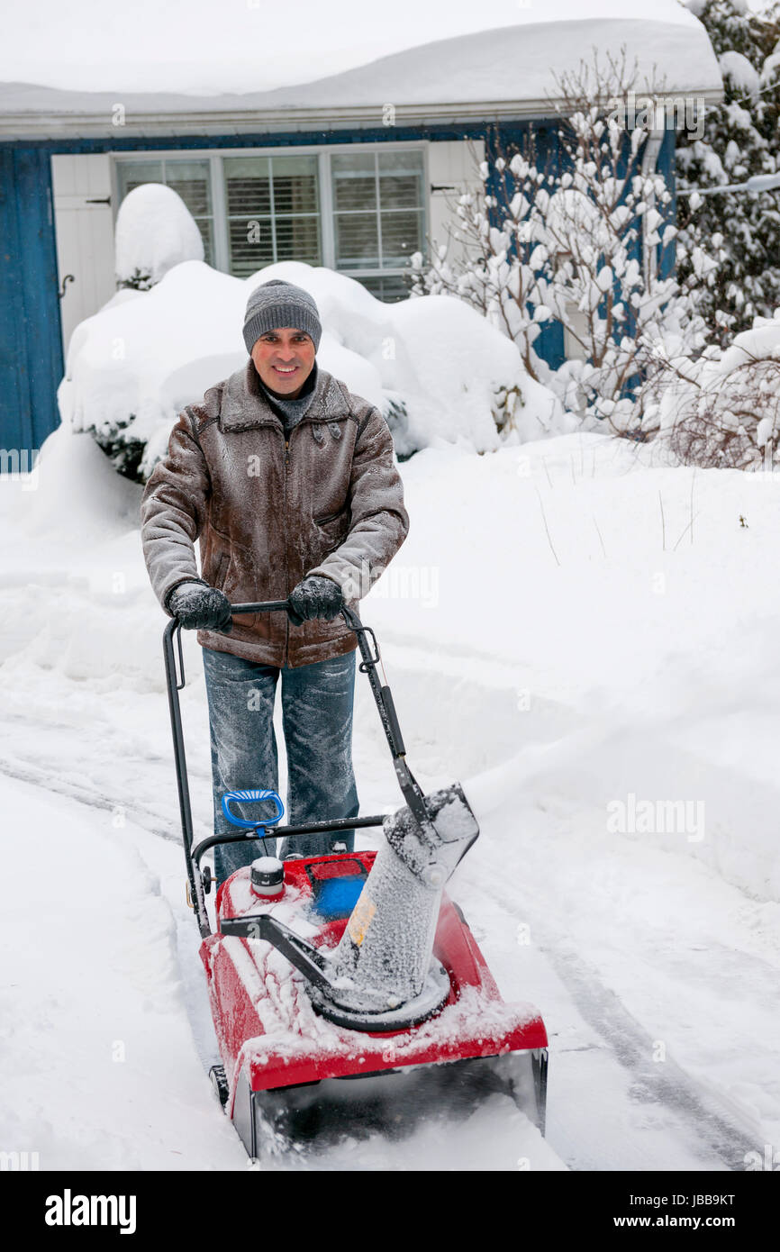 Man using snowblower to clear deep snow on driveway near residential