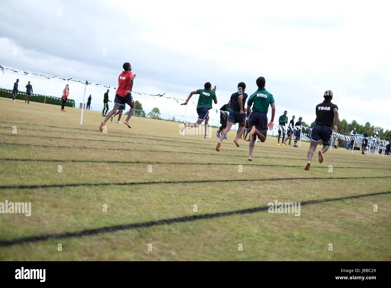 Students sprint barefoot athletic race on grass track in Kenya Stock Photo