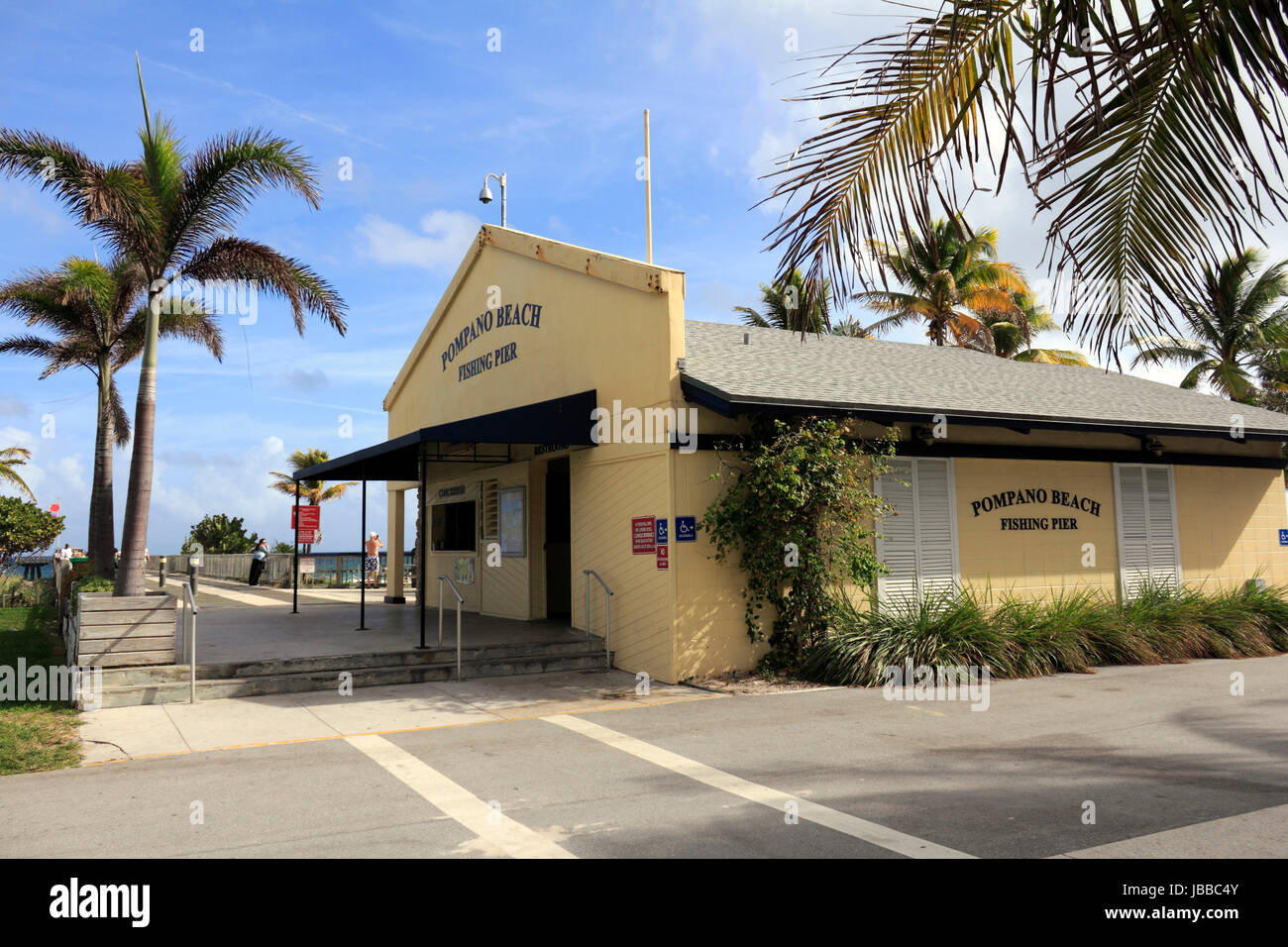 POMPANO BEACH, FLORIDA - DECEMBER 22, 2013: Entrance to wooden 1,000 foot length Pompano Beach Municipal Fishing Pier with concession stand and restrooms building on the right on a sunny tropical day. Stock Photo