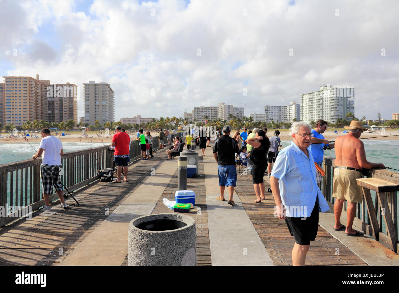 POMPANO BEACH, FLORIDA - DECEMBER 22, 2013: Many people fishing from the very long wood and cement Pompano Beach Municipal Fishing Pier with a view of the beach, bathers and buildings on the coast. Stock Photo