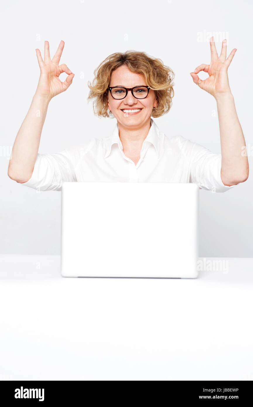 Corporate lady showing excellent gesture to camera sitting in front of ...