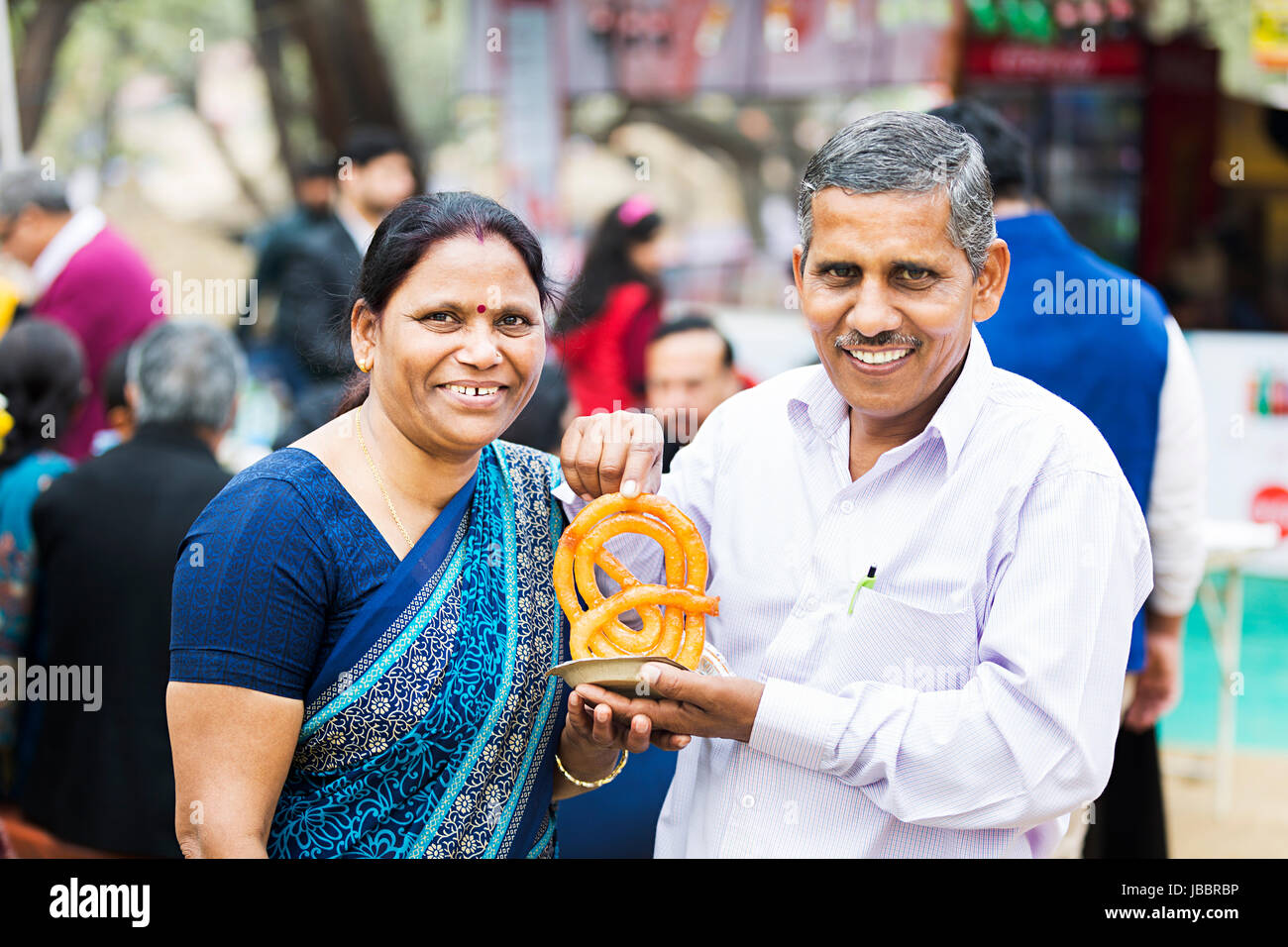 Happy 2 indian Senior Couple Eating Jalebi Fair In Suraj Kund Enjoying Stock Photo