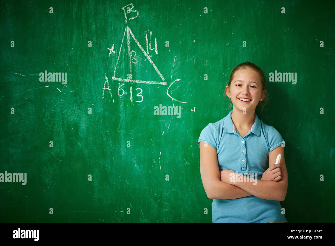 Portrait of clever schoolgirl with piece of chalk standing by the blackboard Stock Photo