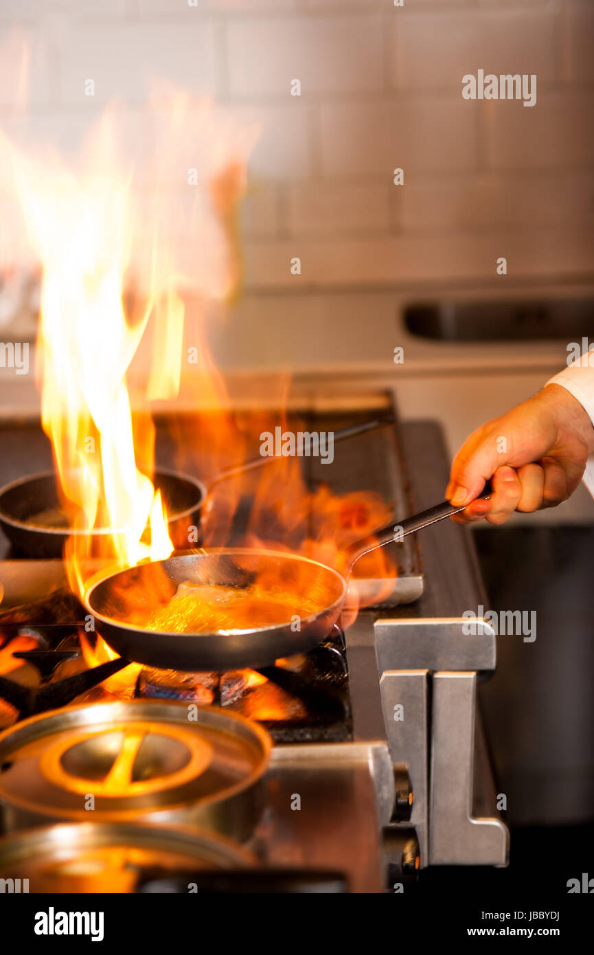 Chef cooking with flame in a frying pan on a kitchen stove Stock Photo ...