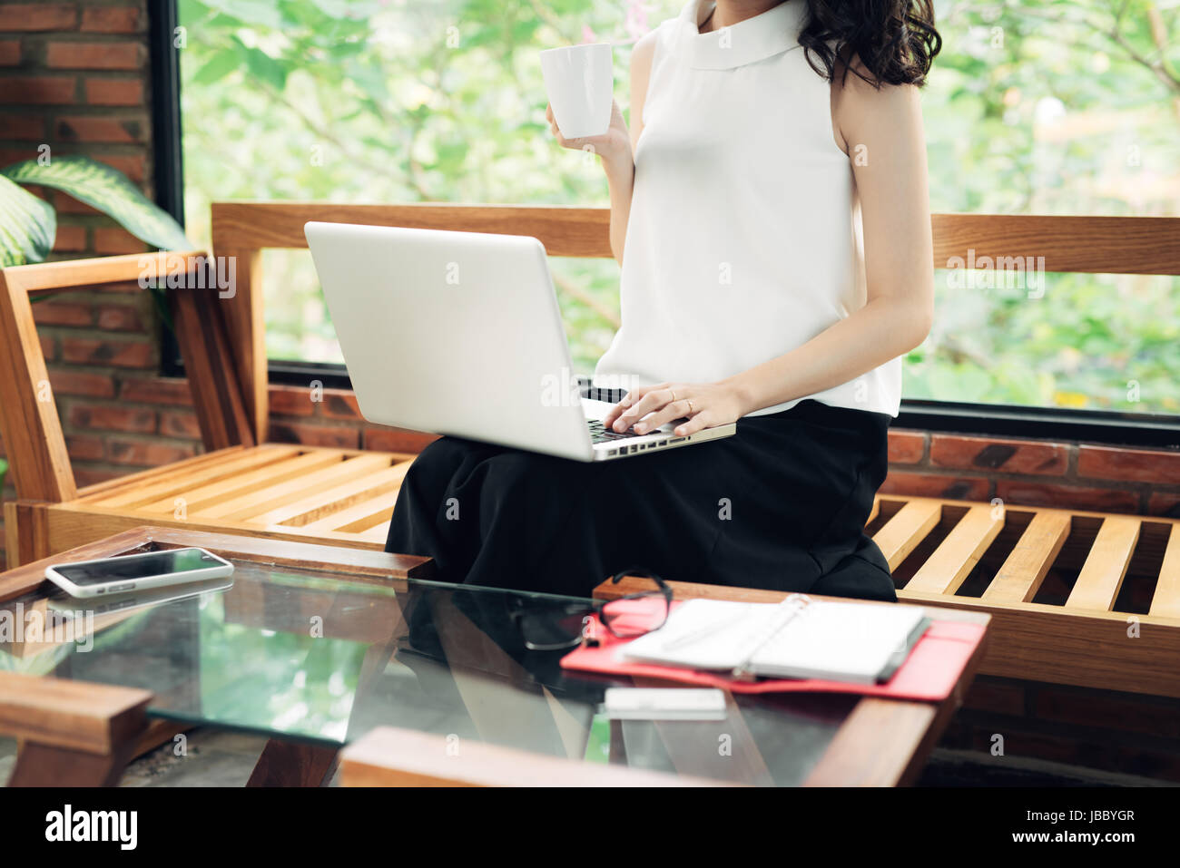 Confident young asian woman in smart casual wear shopping online while sitting near window in creative office or cafe Stock Photo