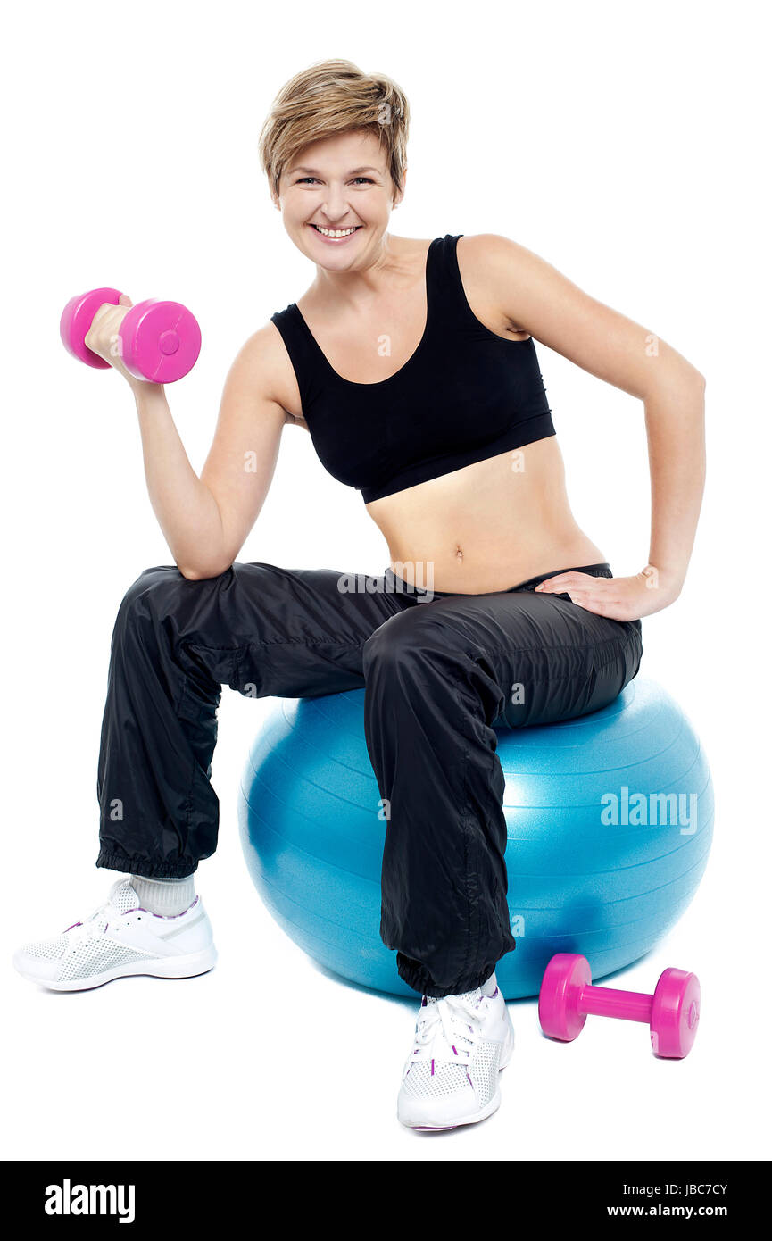 Woman seated on fitness ball doing dumbbells. Smiling at camera Stock ...