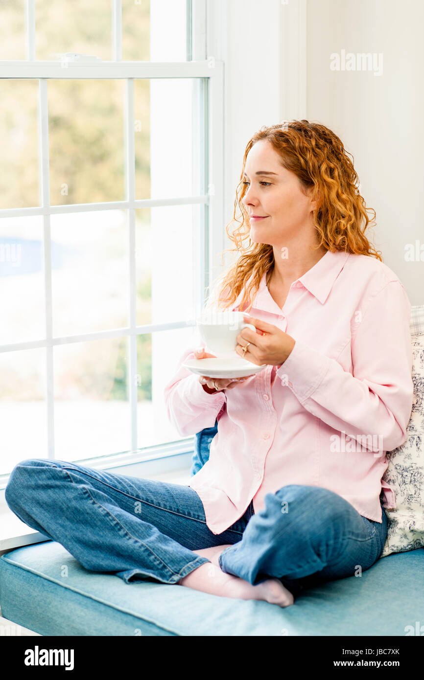 Smiling caucasian woman relaxing on couch by window holding cup of ...