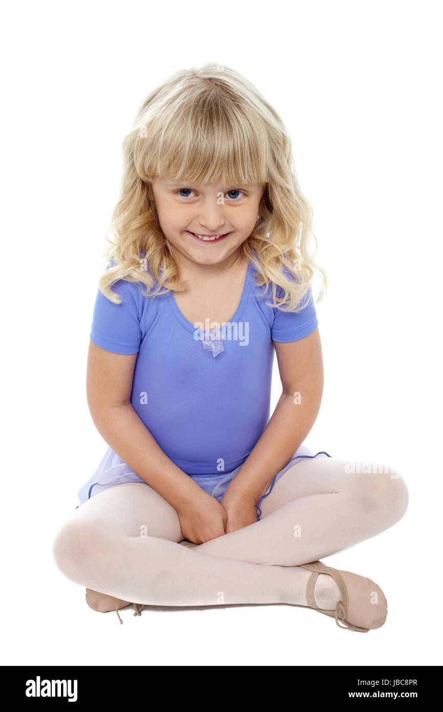 Adorable kid sitting with crossed legs on the floor. Cutely smiling at the camera. Stock Photo