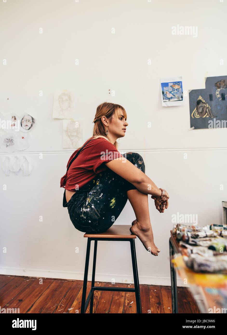 Side view of young woman painter sitting on stool in her studio. Female  artist in her workshop Stock Photo - Alamy