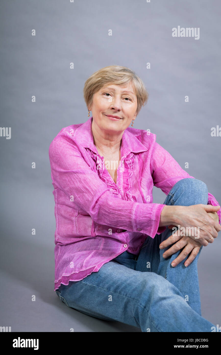 glückliche ältere frau seniorin mit hellen haaren und falten mit rosa bluse vor grauem hintergrund gesund Stock Photo