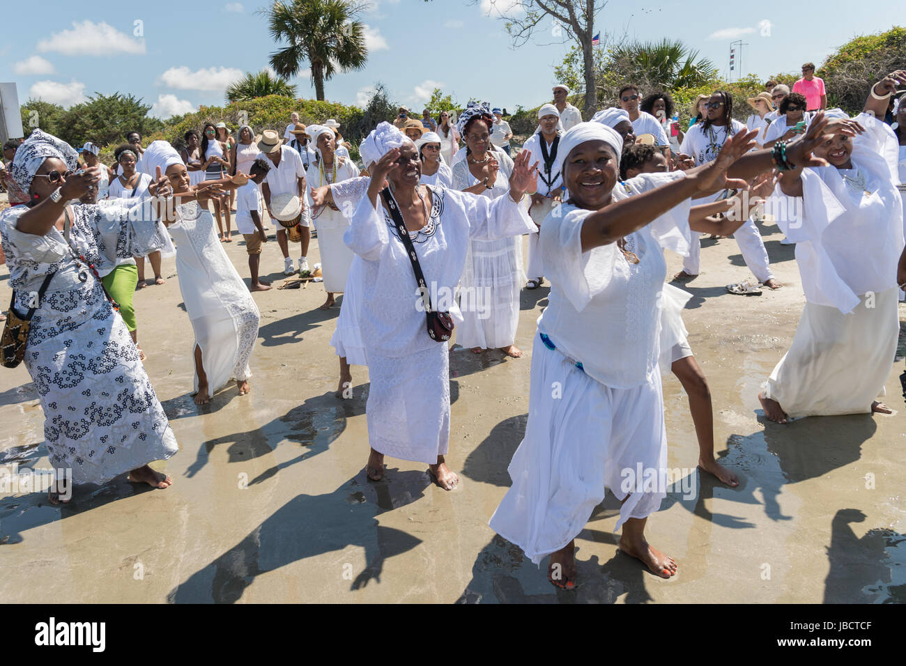 Descendants of enslaved Africans brought to Charleston in the Middle Passage dance to honor their relatives lost during a remembrance ceremony along the ocean front June 10, 2017 in Sullivan's Island, South Carolina. The Middle Passage refers to the triangular trade in which millions of Africans were shipped to the New World as part of the Atlantic slave trade. An estimated 15% of the Africans died at sea and considerably more in the process of capturing and transporting. The total number of African deaths directly attributable to the Middle Passage voyage is estimated at two million Africans. Stock Photo