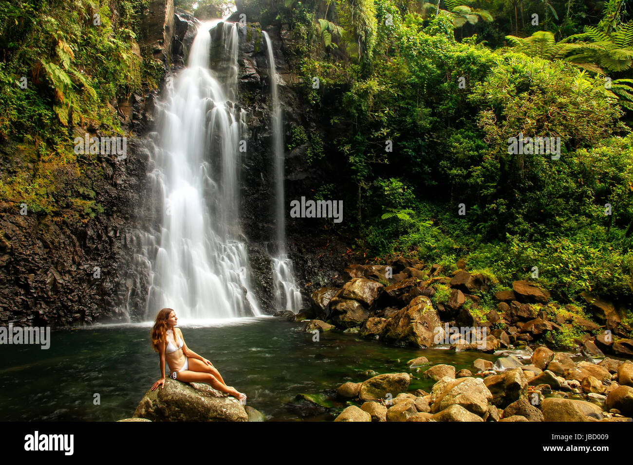 Young woman in bikini sitting by Middle Tavoro Waterfalls in Bouma National Heritage Park on Taveuni Island, Fiji. Taveuni is the third largest island Stock Photo