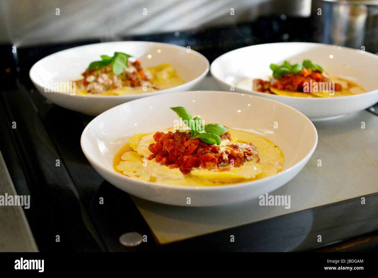 italian ravioli, creamy yellow sauce and green basil leaves in chefs kitchen. Stock Photo