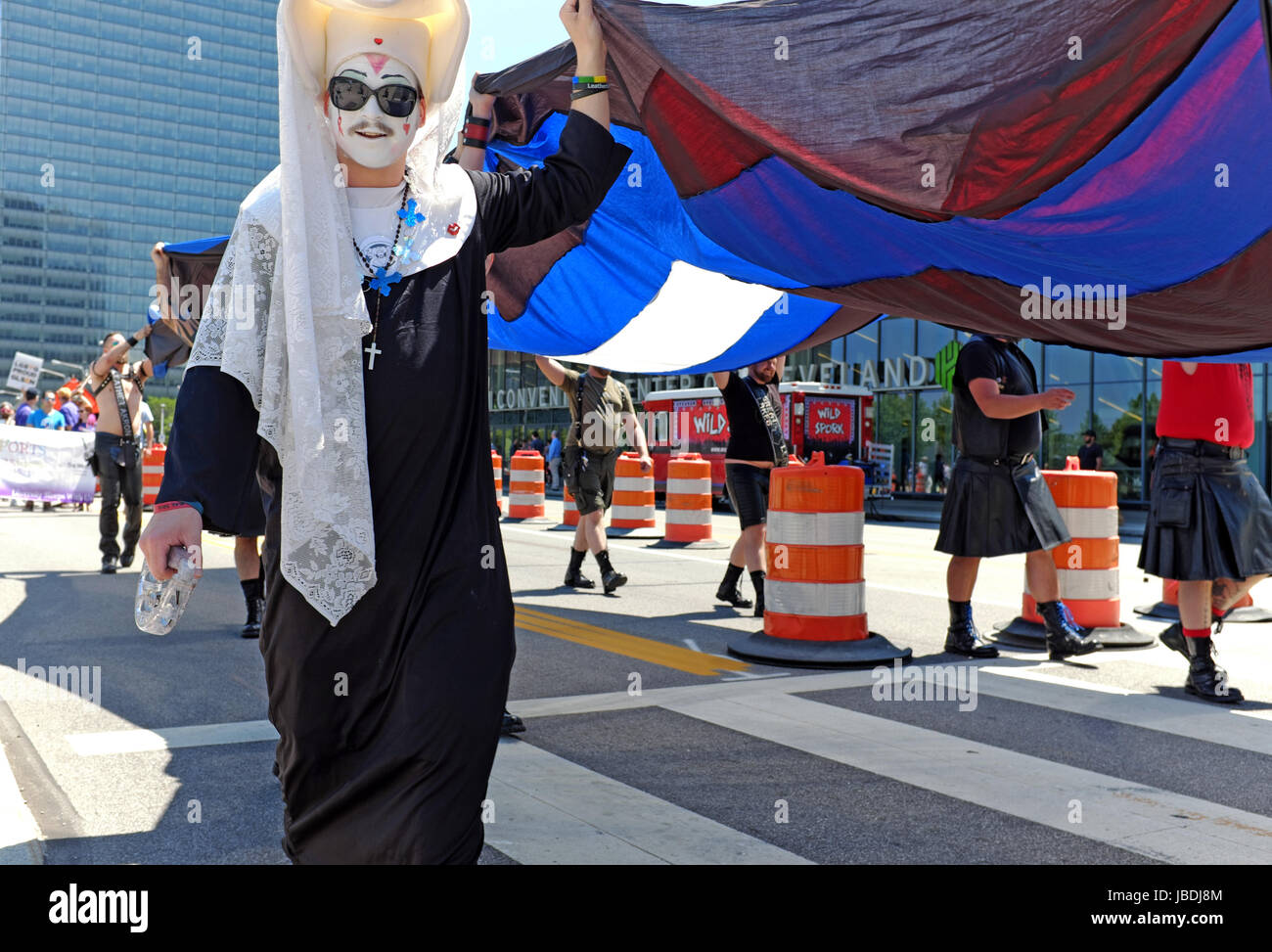 A Sister of Perpetual Indulgence helps carry a large version of the Leather Pride Flag during an LGBT Pride March in downtown Cleveland, Ohio, USA. Stock Photo