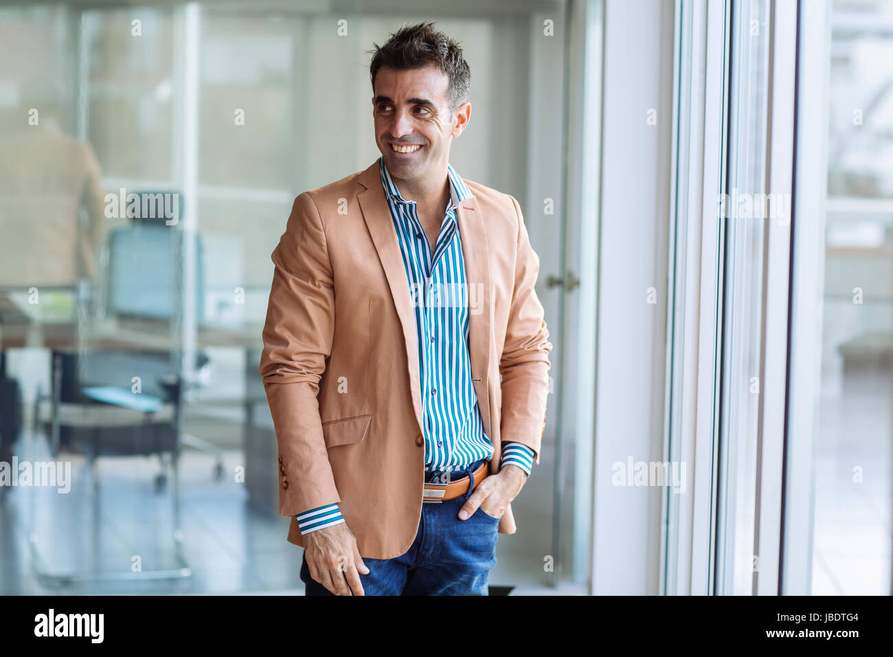 A 35 - 40 years old man caucasian dark hair cool modern look casual in an informal shirt, blazer and jeans in an office, medium long shot Stock Photo